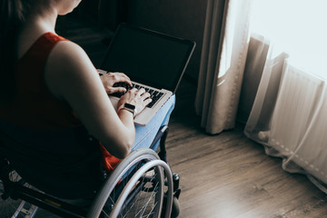 Woman in a wheelchair at home with a laptop on her lap, hand close up, unrecognizable man.