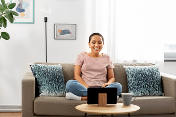 Wall Mural - people, technology and leisure concept - happy young african american woman sitting on sofa with tablet pc computer and watching movie at home