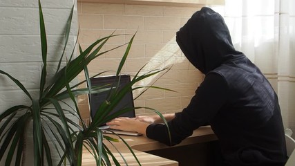 Young anonymous hacker woman in black hoodie is typing on the keyboard
