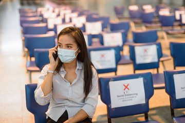 Wall Mural - Young Asian tourist woman with mask talking on the phone while sitting with distance at the airport