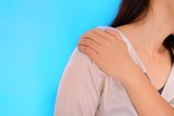 Fototapeta  - An upper mid section shot of a woman with should pain, grabbing and massaging it with her left hand. Light blue plain background.