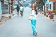 © etemwanich - her hipster style a smile happy girl in good morning time on the road with blur village by her wearing shirt white and jeans wide leg style