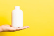 Close up of cosmetics bottle in female hand at yellow background with copy space