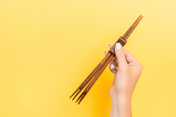 Wall Mural - Female hand holding chopsticks on yellow background. Sushi concept with empty space for your idea