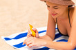 © sosiukin - Beautiful lady is sunbathing on the towel on the sand at the beach and protects her hands with sunblock