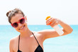 © sosiukin - Young woman is holding a bottle of sunblock for body at the sea background