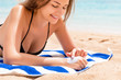 © sosiukin - Cute and smiling woman is applying sunscreen on her hand with the finger sunbathing on the towel at the beach