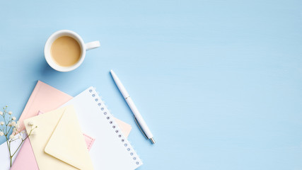 Wall Mural - Feminine workspace with paper notebook, envelope, flowers, cup of coffee on blue background. Stylish home office desk table, flat lay, top view