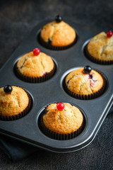 Various homemade muffins in a baking dish with berries, chocolate and mint on a dark background top view copy space.