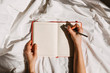 © Bostan Natalia - Hands holding an open blank notebook and a pen on bed background.