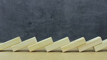 Social Distance During A Pandemic Concept. Side View Of Falling Wooden Blocks Lined Up On A Dark Background. The Principle Of Dominoes. Symbolic Illustration Of The Importance Of Social Distance