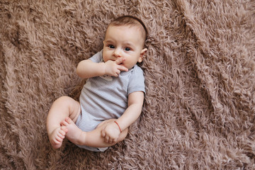 portrait of a child 4 months old lying on the bed and looking. Charming child with dark eyes lying on back, portrait of baby boy