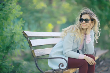 Wall Mural - adult girl sitting on a bench in the park / beautiful model woman resting on a bench, cheerful happy girl