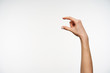Side view of young fair-skinned lady's raised hand measuring invisible items with fingers while being isolated against white background. Hand gesturing concept