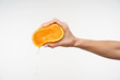 Side view of young attractive lady's hand being raised while pressing half of orange and squeezing juice from it, isolated against white background