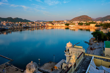 Fototapete - View of famous indian hinduism pilgrimage town sacred holy hindu religious city Pushkar amongst hills with Brahma mandir temple, lake and traditional Pushkar ghats at dusk sunset. Rajasthan, India