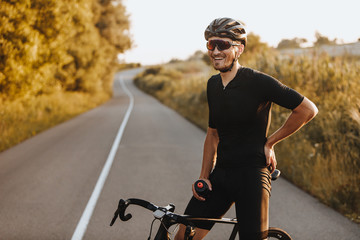 cheerful bearded man in activewear, black helmet and sport glasses sitting on bike and looking on ca