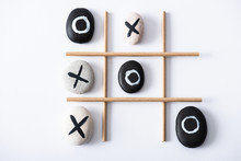 Top View Of Tic Tac Toe Game With Grid Made Of Paper Tubes, And Pebbles Marked With Naughts And Crosses On White Surface