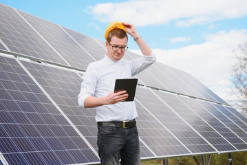 Portrait of man with a tablet in his hands standing near the solar panels station. Green ecological power energy generation. Solar station development concept. Home construction.