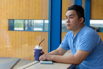 Young handsome overweight Asian man thinking at the coffee shop