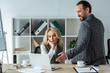 © LIGHTFIELD STUDIOS - Smiling businessman pointing with hand at laptop near businesswoman at table