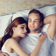 © vgstudio - Portrait of young happy hugging couple laying on the bed, at home. Love, relationship, dating, bedtime concept picture. Square composition.