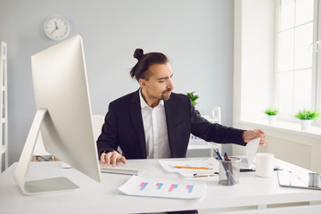 Wall Mural - Businessman in a black jacket works. Analyzes at the computer in the office.