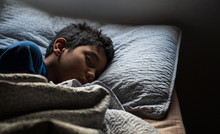 Hispanic Young Boy Sleeping With Head Over Pillow At Bed