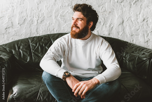 Fotomural Portrait of handsome bearded man looking away and sitting on sofa