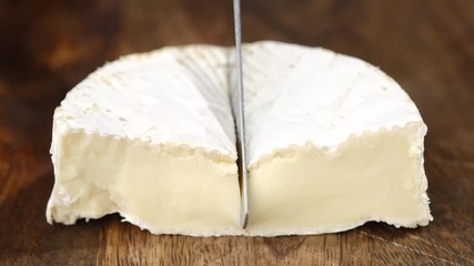 Wall Mural - cutting soft cheese camembert or brie with knife closeup. creamy soft cheese inside. white mold cheeses with soft textures. wooden board