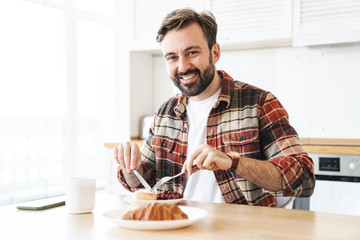 Poster - Portrait of joyful man smiling and eating cake while having breakfast