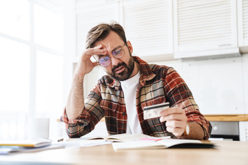 Canvas Print - Portrait of young serious man holding credit card while working at home