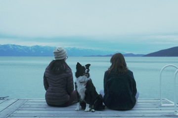 Sisters and their Border Collie dog sitting on a dock