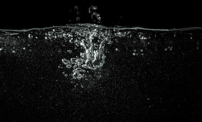  Water pouring into aquarium, black background, detail on dropped liquid creating white bubbles and abstract shapes