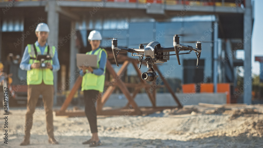 Diverse Team of Specialists Pilot Drone on Construction Site. Architectural Engineer and Safety Engineering Inspector Fly Drone on Commercial Building Construction Site Controlling Design and Quality - obrazy, fototapety, plakaty 