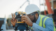 © Gorodenkoff - On the Commercial / Industrial Building Construction Site: Professional Engineer Surveyor Takes Measures with Theodolite, Worker Uses Laptop. In the Background Skyscraper Formwork Frames and Crane