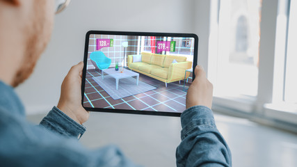 Decorating Apartment: Man Holding Digital Tablet with AR Interior Design Software Chooses 3D Furniture for Home from Online Shop with Shown Prices. Over Shoulder Screen Shot with 3D Render