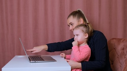 young beautiful blonde and her charming little daughter are shopping online with a laptop and credit card. Shopping in the online store.