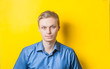 © aeroking - Serious young blond man in a blue shirt on a yellow background. Photo Shoot.