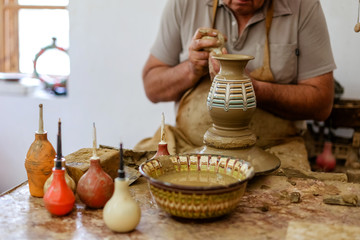 A Potter makes a jug with his hands a vase made of brown clay on a Potter's wheel in a traditional Bulgarian pattern