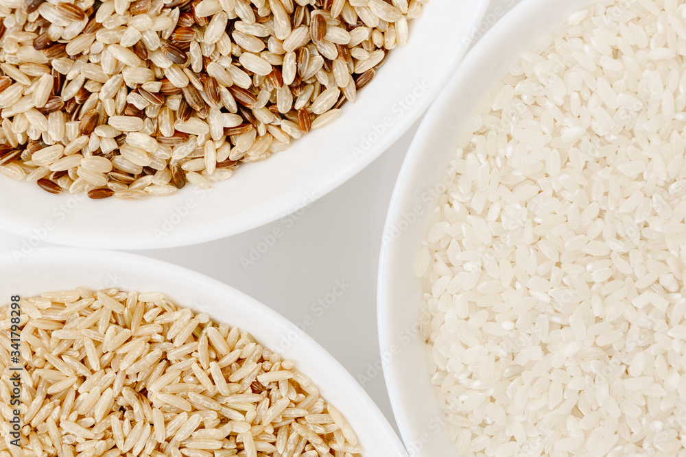 Bowls with different types of raw uncooked rice: brown, red, white ...