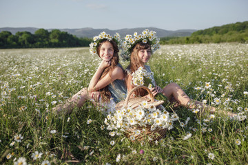 two cute teen girls in denim overalls walk in a daisy field