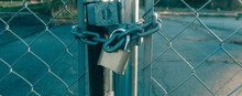 Locked Gate Tethered By Metal Chain And Old Rusty Padlock On Sunshines Background. Wide Photo.