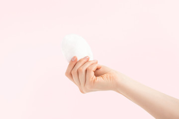 White cosmetic cotton pad in a woman hand on pink background. Make up remover pad, absorbent for micellar water, cotton sponge. Palm facing up. 