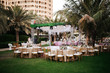 International Wedding outdoor celebration party under palm trees. Served tables on green area in hotel. Landyard. Beige and pink colors. Close-up and wide angle.