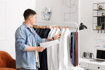 Poster - Male Asian stylist near rack with clothes in studio