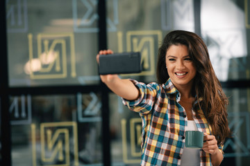 Wall Mural - Young woman at work. Beautiful businesswoman making selfie photo in office.