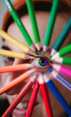 Portrait of a beautiful young woman with a colorful eye in the rainbow. Highlighted by a circle made of pencils as a symbol of art,education and inspiration.