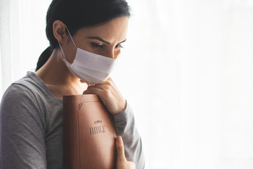 Wall Mural - Portrait of a woman with a surgical mask on her face and a bible held tight to her chest