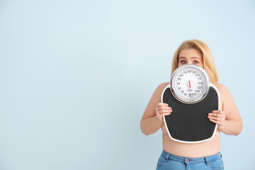 Wall Mural - Troubled overweight woman with scales on color background. Weight loss concept
